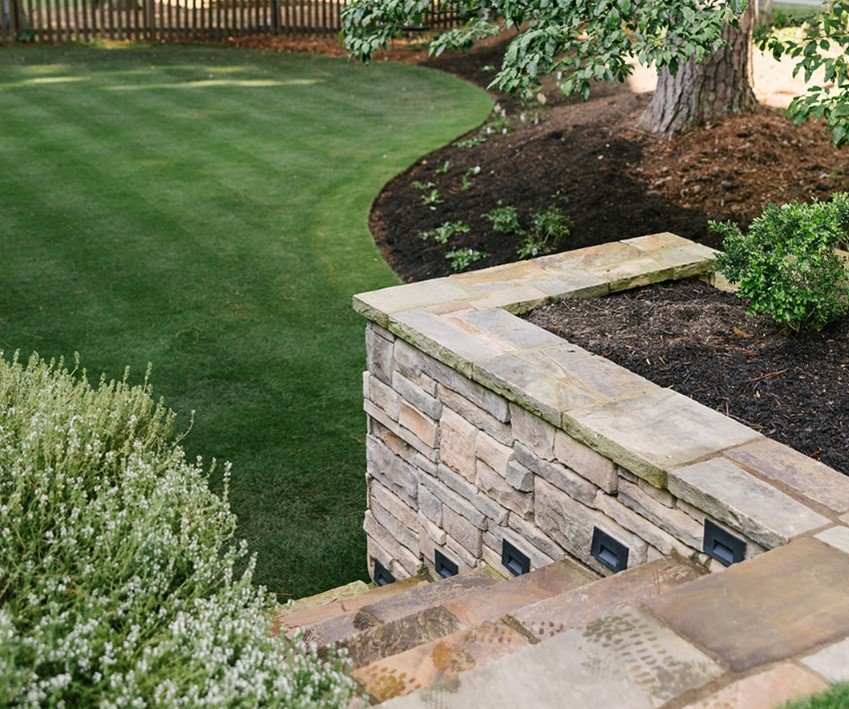 Landscaped yard with a stone retaining wall, steps, and lush greenery in Metro Atlanta